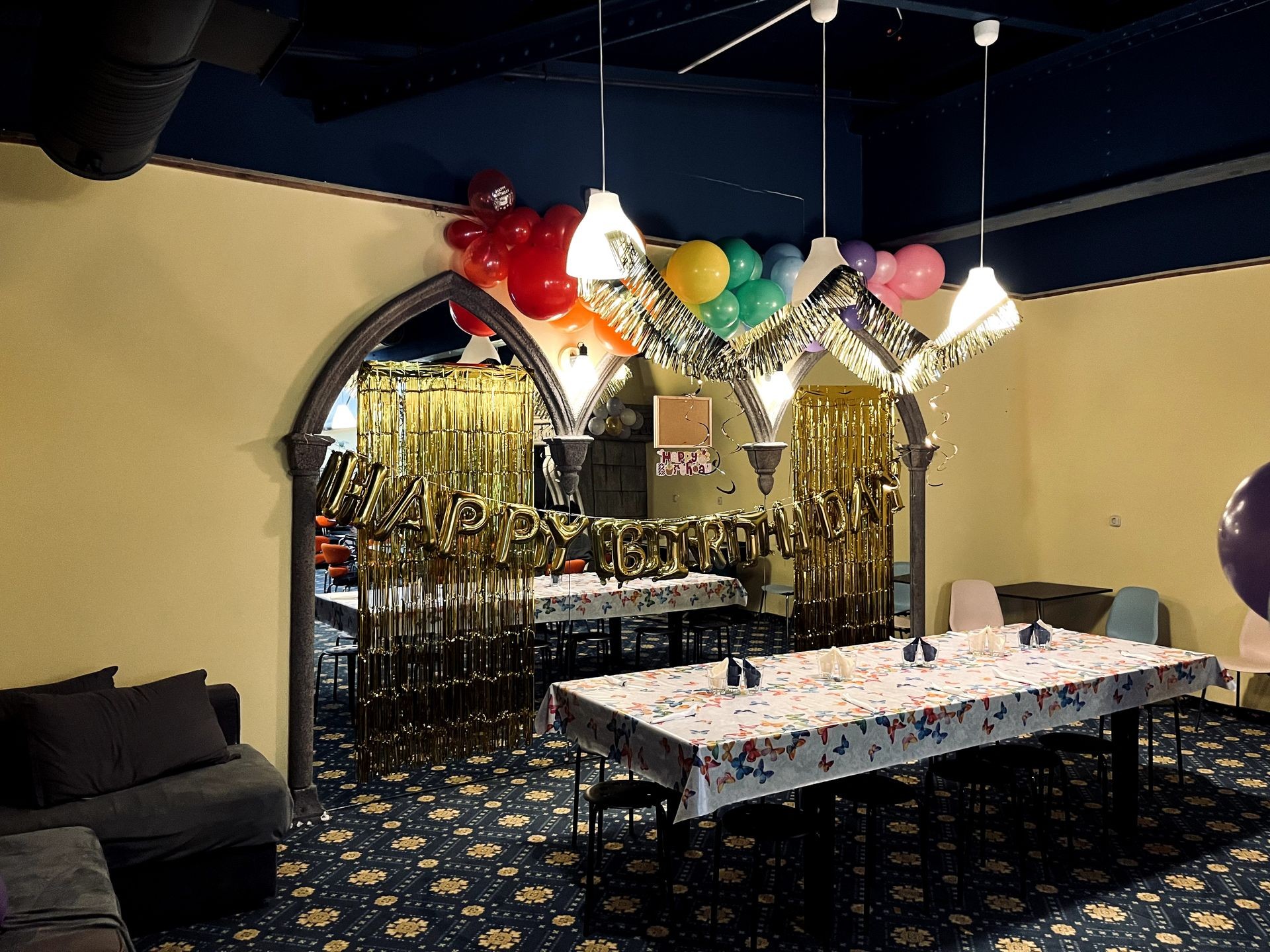 Room decorated with balloons and 'Happy Birthday' banner, tables covered with butterfly tablecloths.