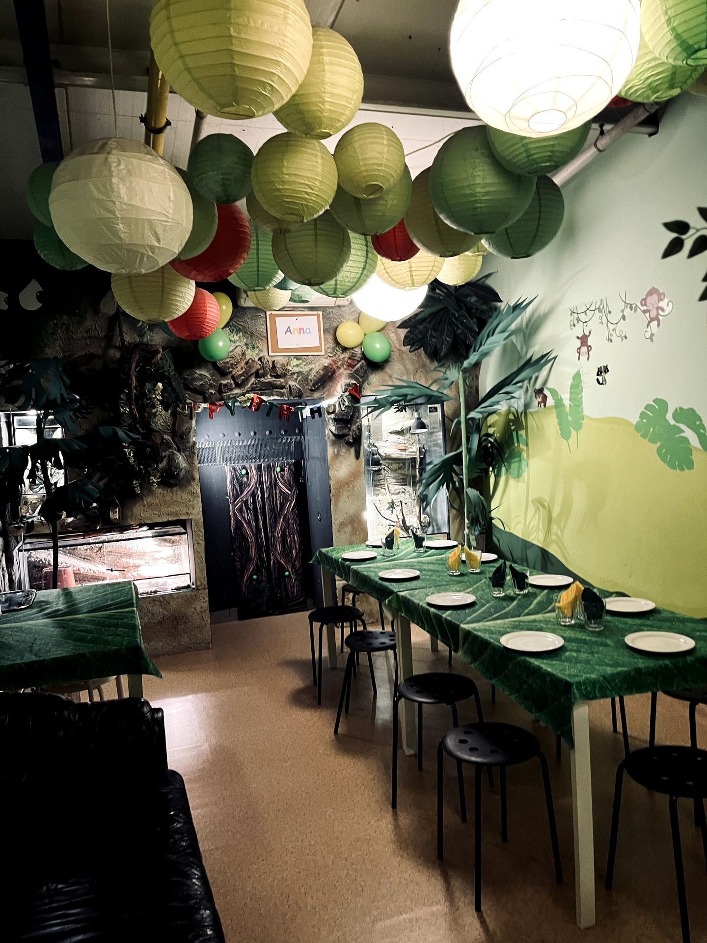 Jungle-themed indoor party room with green paper lanterns and tables set with plates.