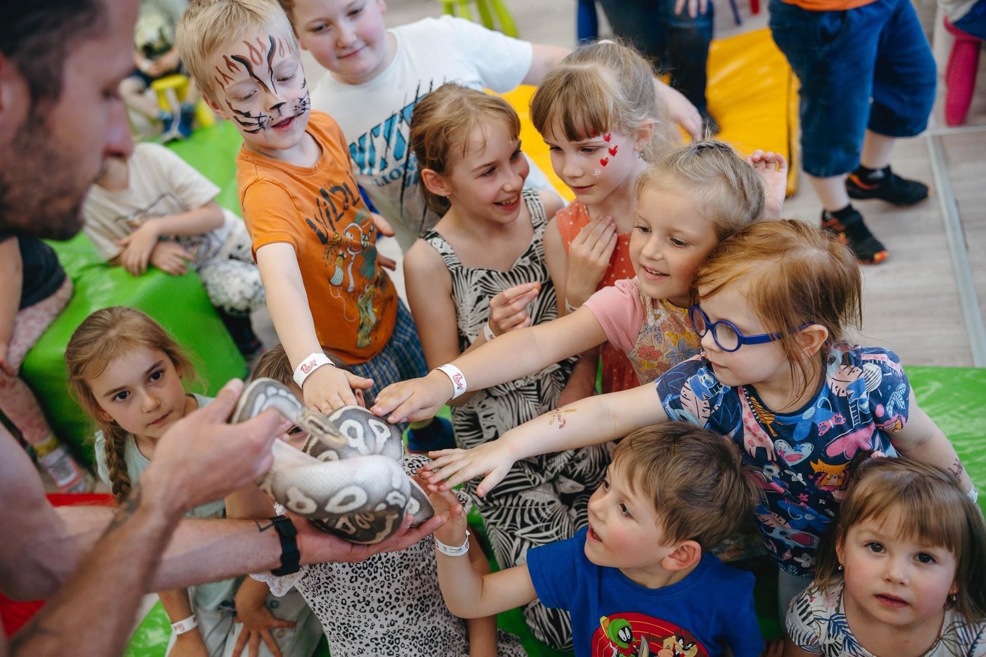 Children reaching out to touch a snake held by an adult during an educational activity.