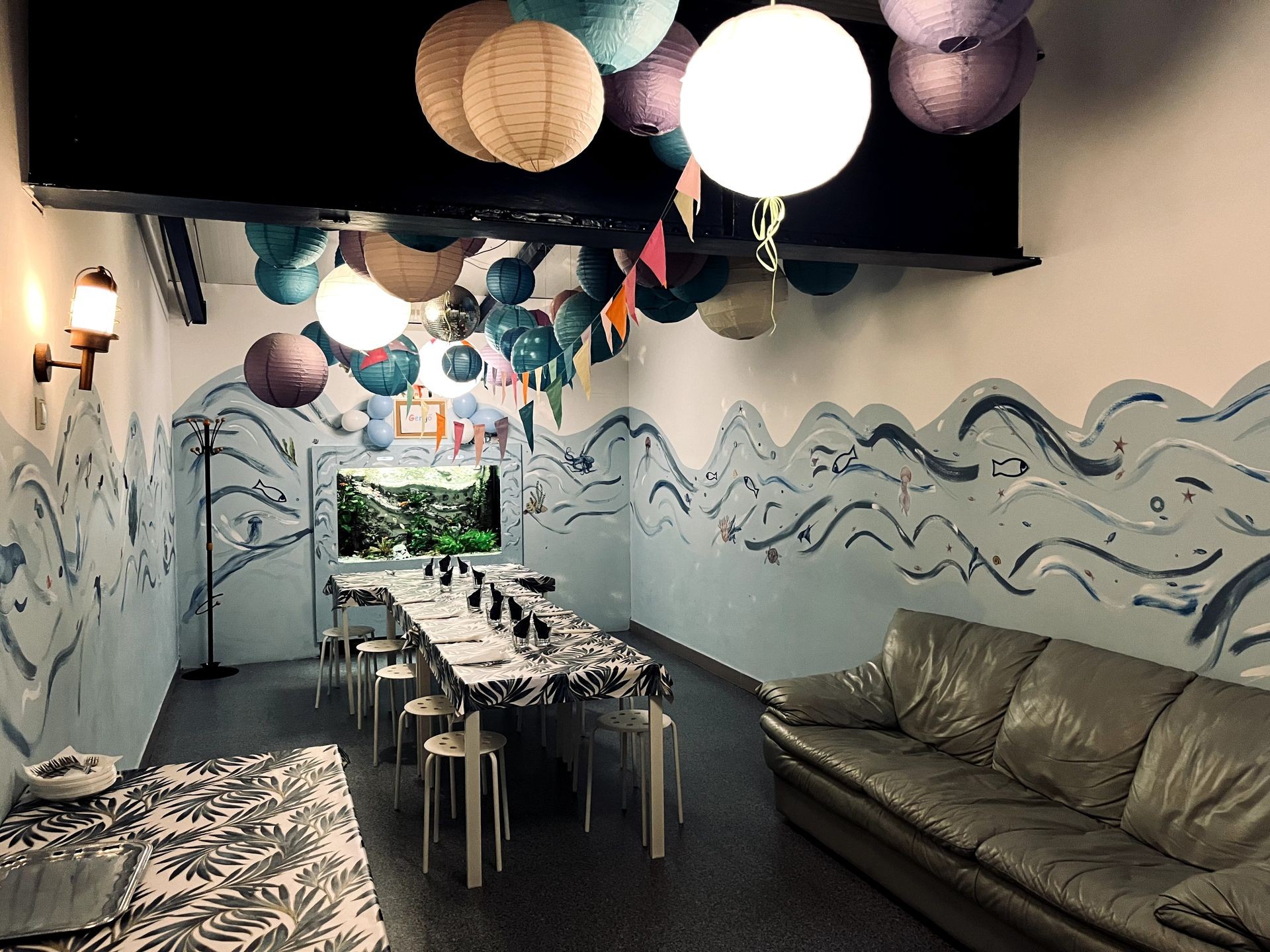 Decorated room with ocean-themed mural, hanging lanterns, and tables set for dining.